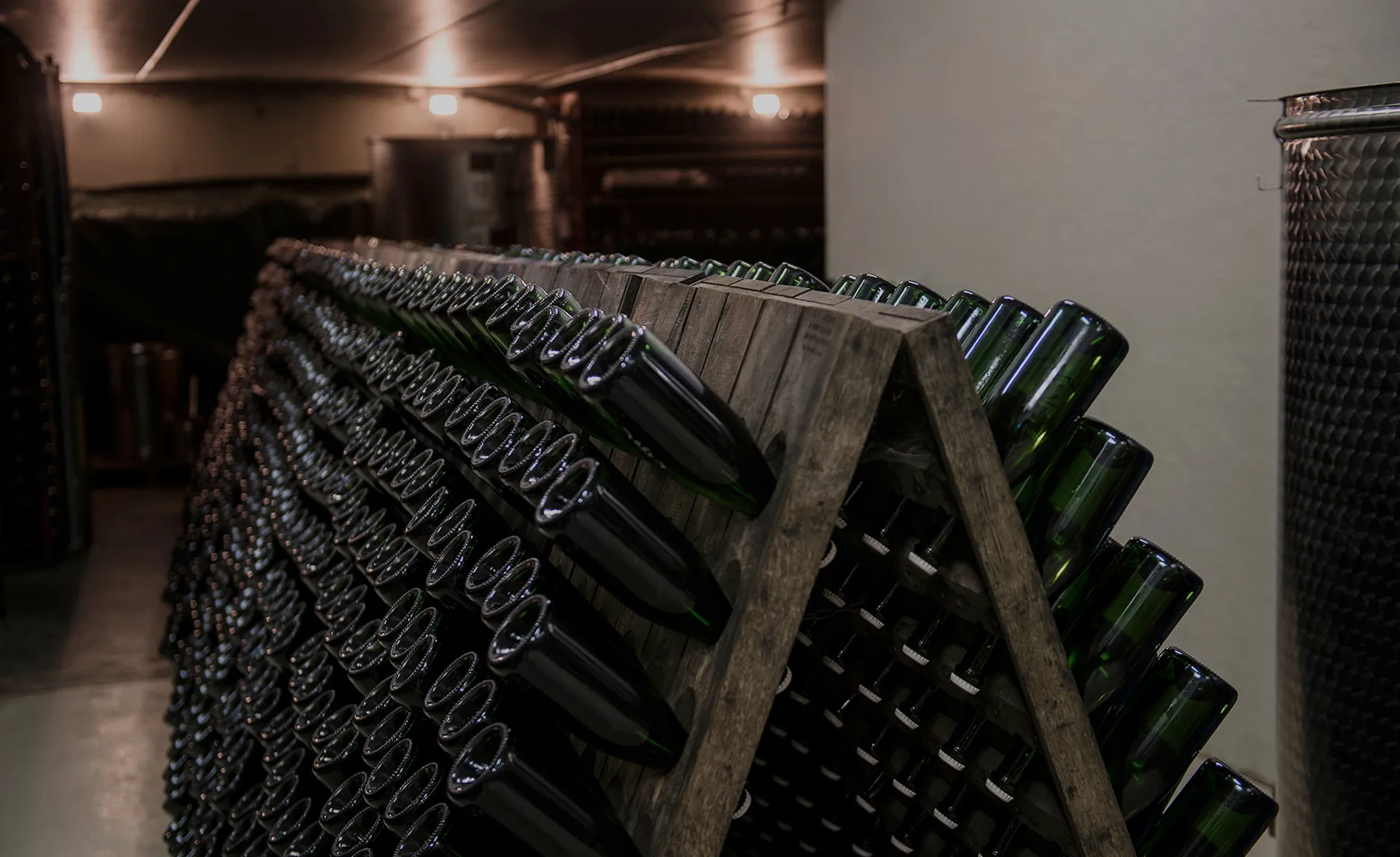 Holz-Rüttelpulte mit hunderten Sektflaschen im Arunda-Produktionskeller, Edelstahltanks im Hintergrund, Mölten