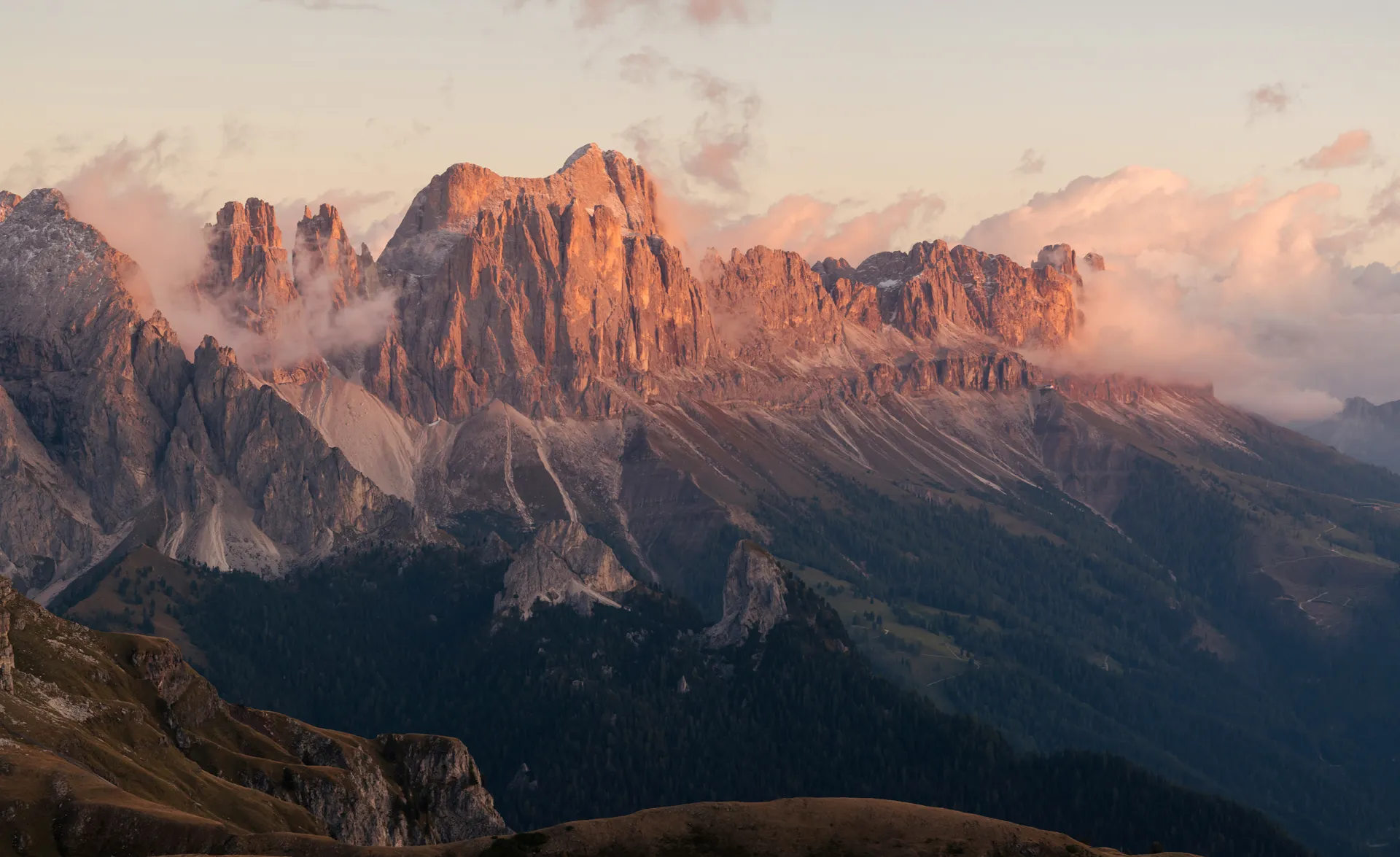 Markante Dolomitengipfel in warmem Alpenglühen bei Sonnenuntergang, grüne Almwiesen im Vordergrund, Südtirol