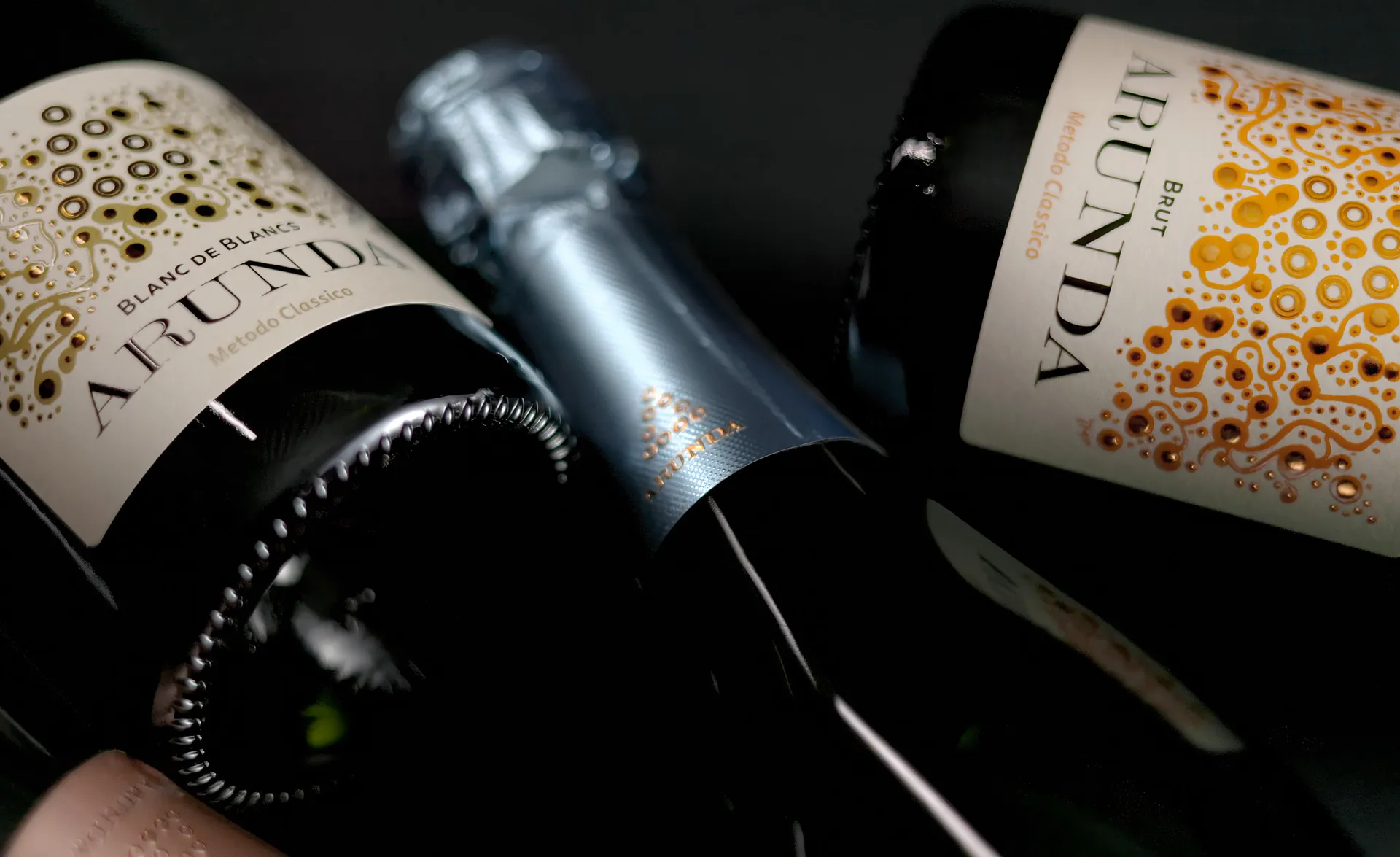 Drei Arunda-Sektflaschen liegend auf schwarzer Fläche, Blanc de Blancs und Brut, kunstvolles Etikettendesign
