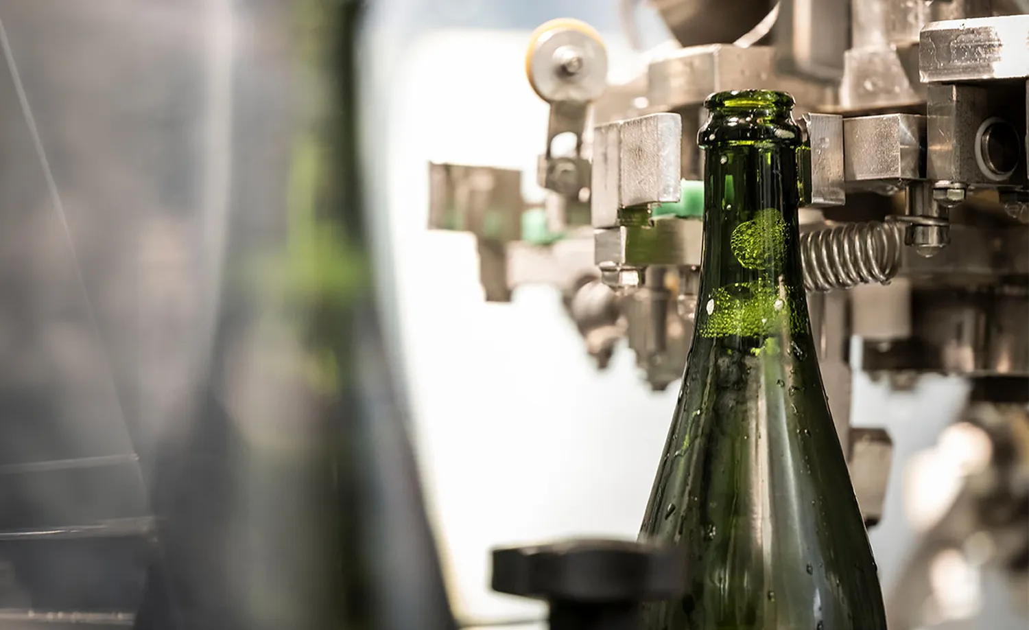 Dunkelgrüne Sektflasche in Edelstahl-Abfüllanlage mit Metallhalterungen und Schutzscheibe, Arunda-Produktion in Mölten