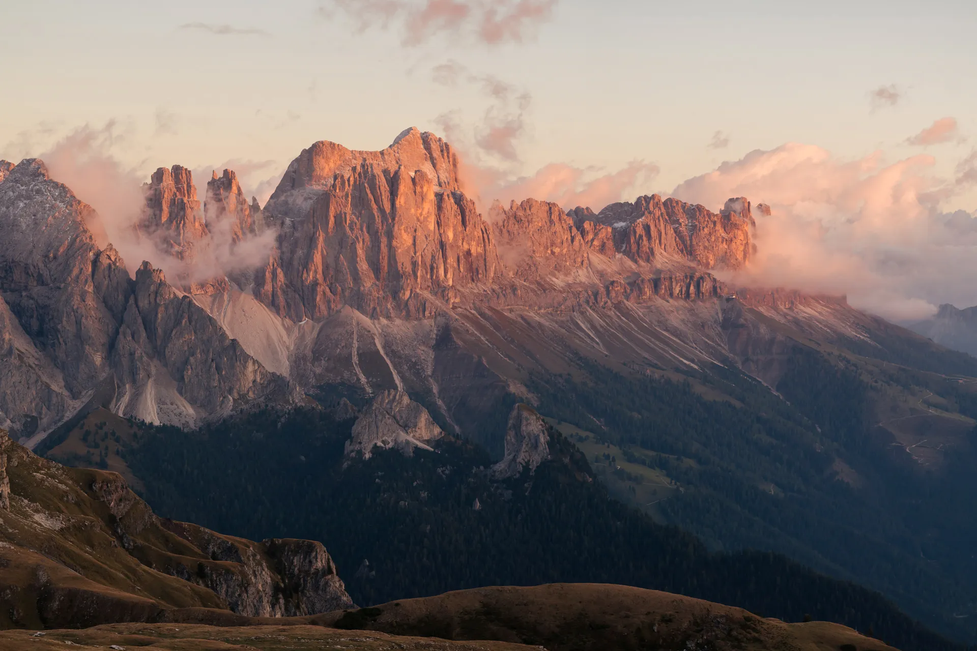 Markante Dolomitengipfel in warmem Alpenglühen bei Sonnenuntergang, grüne Almwiesen im Vordergrund, Südtirol