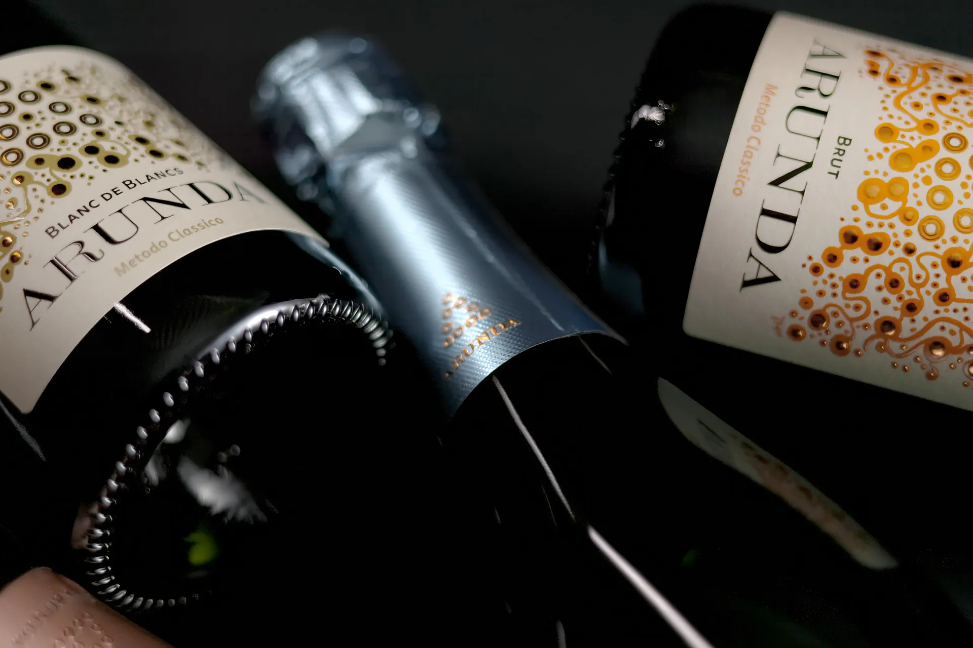 Drei Arunda-Sektflaschen liegend auf schwarzer Fläche, Blanc de Blancs und Brut, kunstvolles Etikettendesign