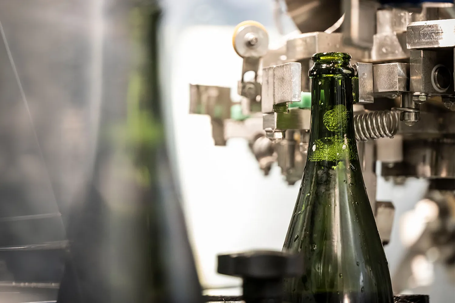 Dunkelgrüne Sektflasche in Edelstahl-Abfüllanlage mit Metallhalterungen und Schutzscheibe, Arunda-Produktion in Mölten