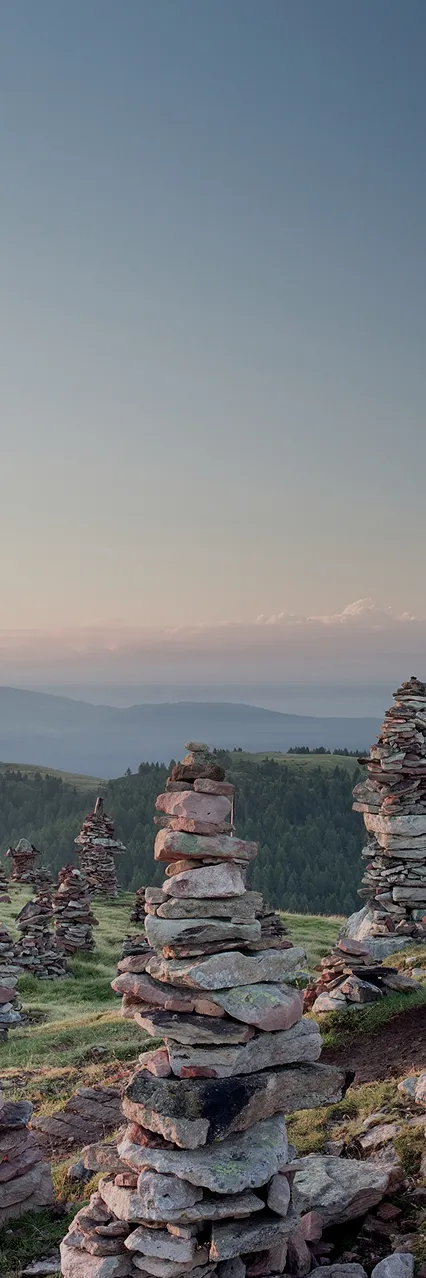 Gestapelte Steinmännchen auf grüner Bergkuppe in den Südtiroler Alpen bei Abenddämmerung nahe Mölten