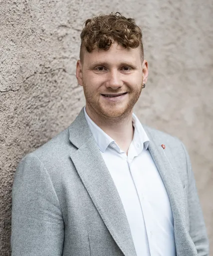 Klemens Schwarzer mit rötlich-blonden Locken in hellgrauem Tweed-Sakko, freundlich lächelnd, Teamportrait