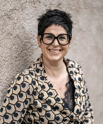 Sonja Mittelberger mit kurzen Haaren und schwarzer Brille in gemusterter Bluse, herzlich lächelnd, Arunda-Teamportrait