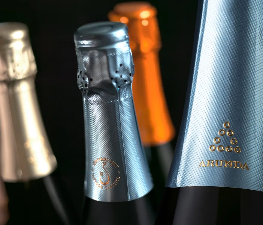 Mehrere Arunda-Sektkapseln in Silber, Orange und Gold mit Prägung Südtirol Sekt, schwarzer Hintergrund