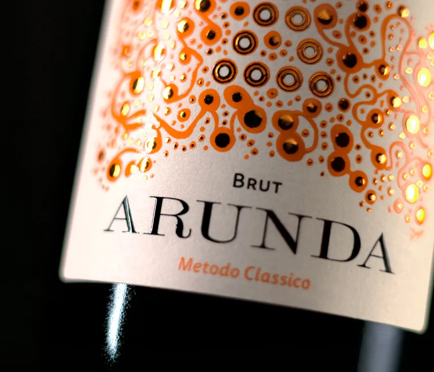 Nahaufnahme Arunda Brut Etikett mit orangefarbenen Blasen-Ornamenten und goldenen Akzenten, schwarzer Hintergrund