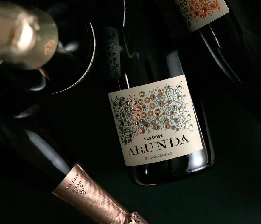 Arunda Pas Dosé Sektflaschen mit Kupfer-Muster-Etikett vor schwarzem Hintergrund, dramatisches Licht