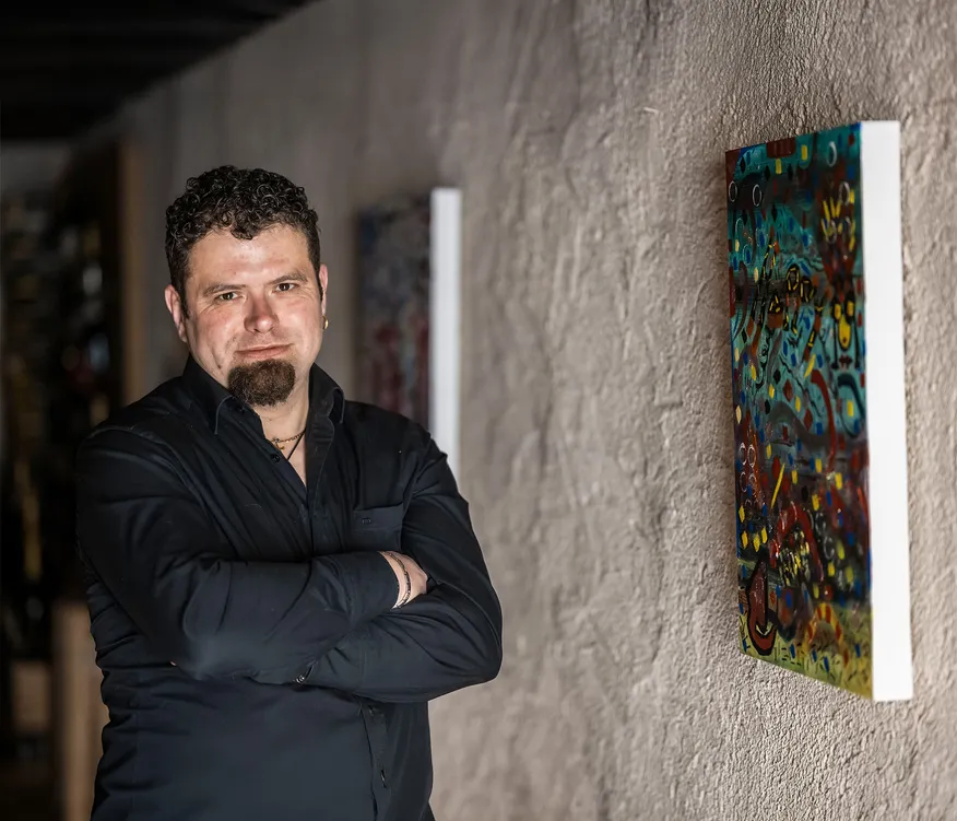 Michael Muggi Reiterer mit verschränkten Armen im Arunda-Kellergang vor farbenfrohem abstrakten Gemälde, dramatisches Licht