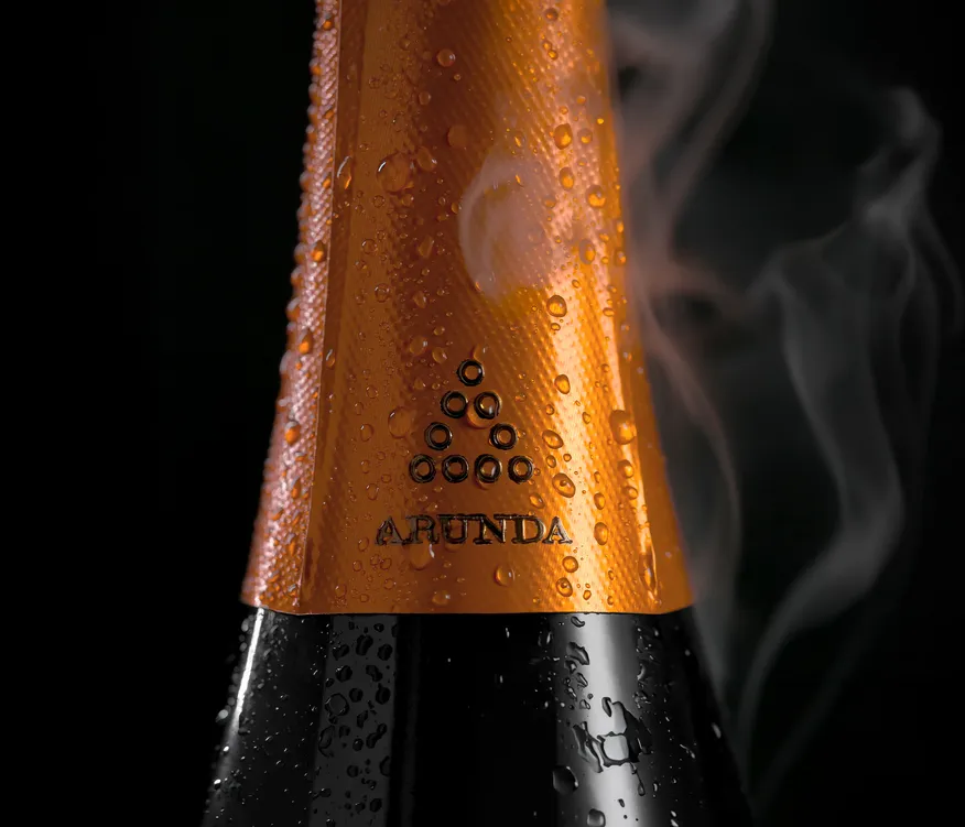 Kupferfarbene Arunda-Flaschenkapsel mit Logo, Kondenswassertropfen und Nebel, schwarzer Hintergrund
