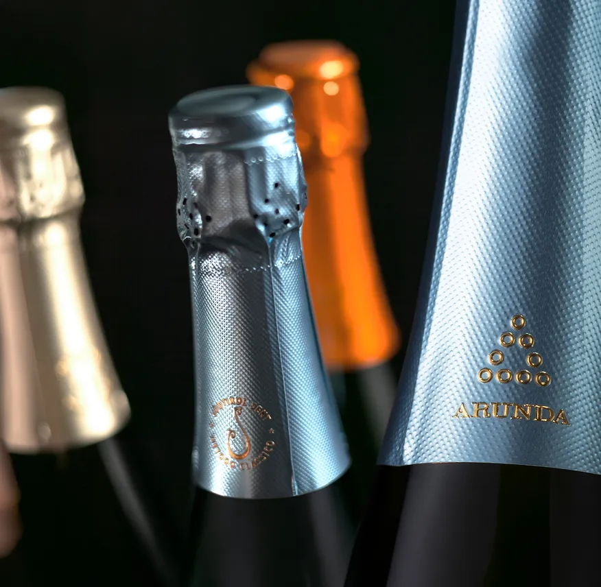 Mehrere Arunda-Sektkapseln in Silber, Orange und Gold mit Prägung Südtirol Sekt, schwarzer Hintergrund