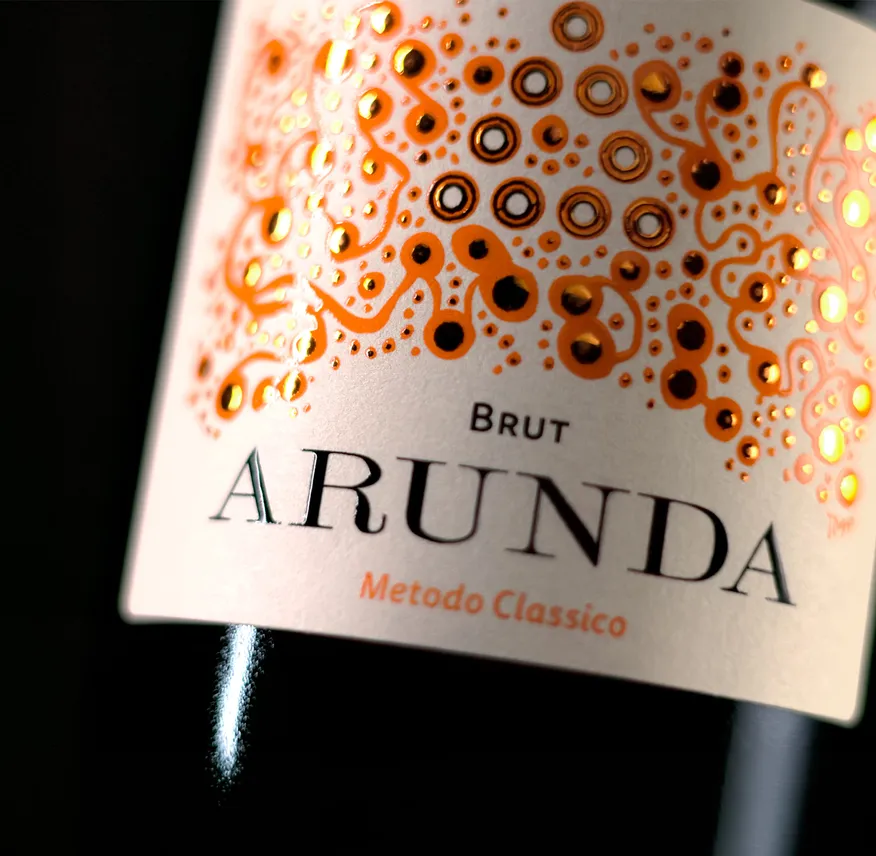 Nahaufnahme Arunda Brut Etikett mit orangefarbenen Blasen-Ornamenten und goldenen Akzenten, schwarzer Hintergrund