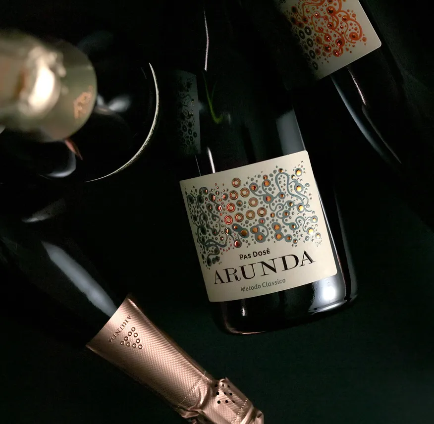 Arunda Pas Dosé Sektflaschen mit Kupfer-Muster-Etikett vor schwarzem Hintergrund, dramatisches Licht